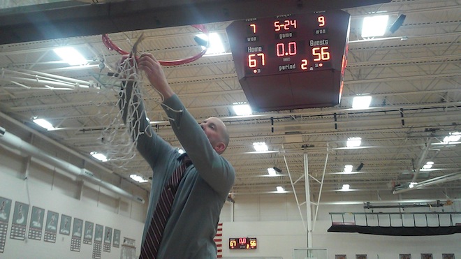 Westosha Central basketball coach James Hyllberg takes down the final threads of the net after the Falcons claimed a Southern Lakes Conference title Friday.