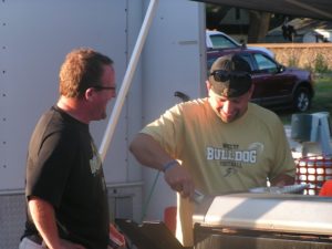 Western Kenosha County Youth Football's Executive Vice President Brent Brenner (left) shares a laugh with Vice President of Tackle Mike Gentile, who is getting food hot off the grill at Silver Lake's Summer Beats (Jason Arndt/The Report).